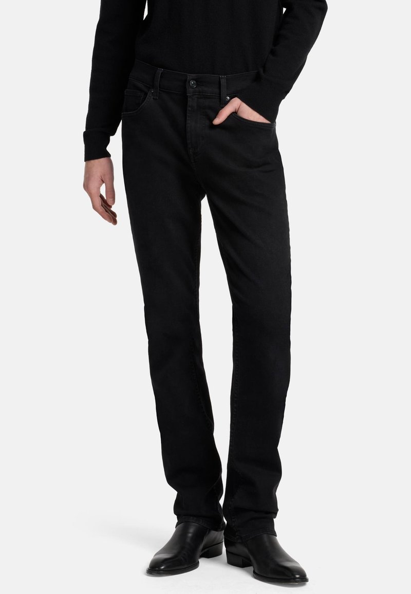 Jeans in denim nero con design a gamba dritta, cinque tasche e dettagli di cucitura minimi. Indossati con una maglietta nera a maniche lunghe e stivali neri.