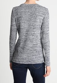 Dlouhý rukáv top v měkké, melírované šedé pletenině s kulatým výstřihem a přiléhavým střihem, kombinovaný s tmavými džíny. Hladká textura s jemným vzorem.