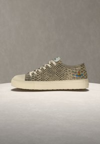 Αθλητικό παπούτσι χαμηλού κορμού με μπεζ μοτίβο φιδιού, κρεμ σόλα και κορδόνια, και ένα μικρό πολύχρωμο λογότυπο κοντά στη φτέρνα σε ουδέτερο φόντο.