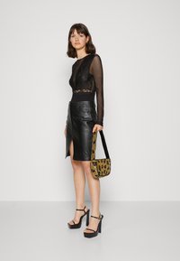 Blusa negra transparente de manga larga con detalles de encaje, combinada con una falda lápiz de cuero negra con una abertura lateral. Acentuada con un bolso amarillo de diseño y tacones de plataforma.