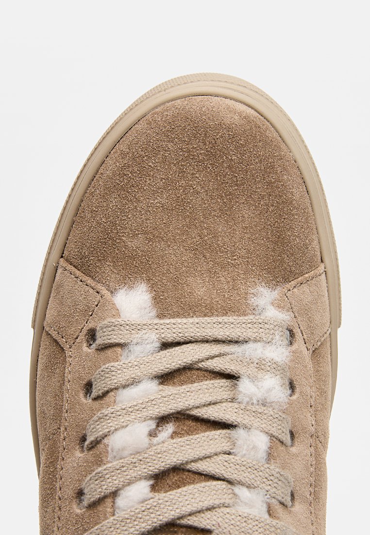 Hellbrauner Wildledersneaker mit abgerundeter Spitze, texturiertem Obermaterial, flachen Schnürsenkeln und einer beigefarbenen Gummisohle mit weißen Akzenten.