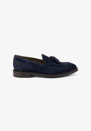 Mocassini in suede azul navy con dettaglio a nappina, caratterizzati da una punta rotonda, accenti di cuciture laterali doppie e una suola marrone a contrasto.