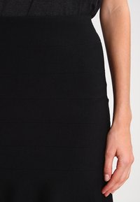 Černá přiléhavá sukně s horizontální žebrovanou strukturou. Hladká látka, délka ke kolenům a jemně rozšířený lem. Charakteristická svou jednobarevností.