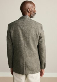 Sacou cu model houndstooth în gri și maro, realizat din lână texturată, cu un șliț central și manșete cu nasturi. Vedere din spate.