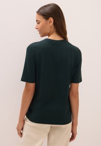 Dunkelgrünes T-Shirt mit kurzen Ärmeln und Rundhalsausschnitt, aus weichem Stoff. Nahtdetails an den Schultern und eine lockere Passform.
