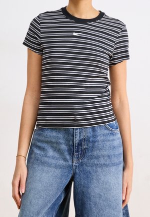 Personne portant un t-shirt à manches courtes rayé noir et blanc avec un petit logo et un jean en denim bleu taille haute.