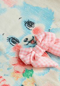 Textiel met een kleurrijke illustratie van een fluffy blauw dier met grote ogen, vergezeld van een roze ruitjesstrik.