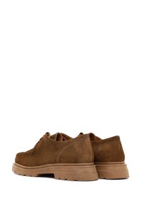 Brown suede lace-up shoes with chunky rubber soles, visible stitching, and a casual, rugged design shown from the back and side angle.
