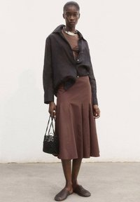 Schwarzes Leinen-Hemd mit Knöpfen, brauner taillierter Rock, gewebte schwarze Handtasche und schwarze strukturierte Slipper. Einfaches Design, neutrale Farben.
