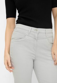 Pantalons gris clair au toucher lisse, avec des passants de ceinture, une fermeture à bouton et deux poches avant. Portés avec un haut noir à côtes.