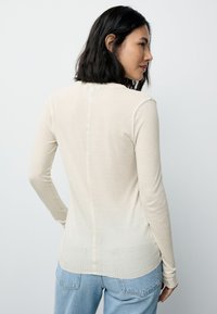 Bluză bej cu mâneci lungi, cu model reiat și croială mulată. Are o cusătură dreaptă la spate și tiv ușor curbat. Textură moale, detalii minimaliste.