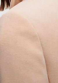 Tela texturizada de color rosa suave de una chaqueta a medida, con un cuello estructurado y líneas limpias, con costuras sutiles visibles en la superficie.