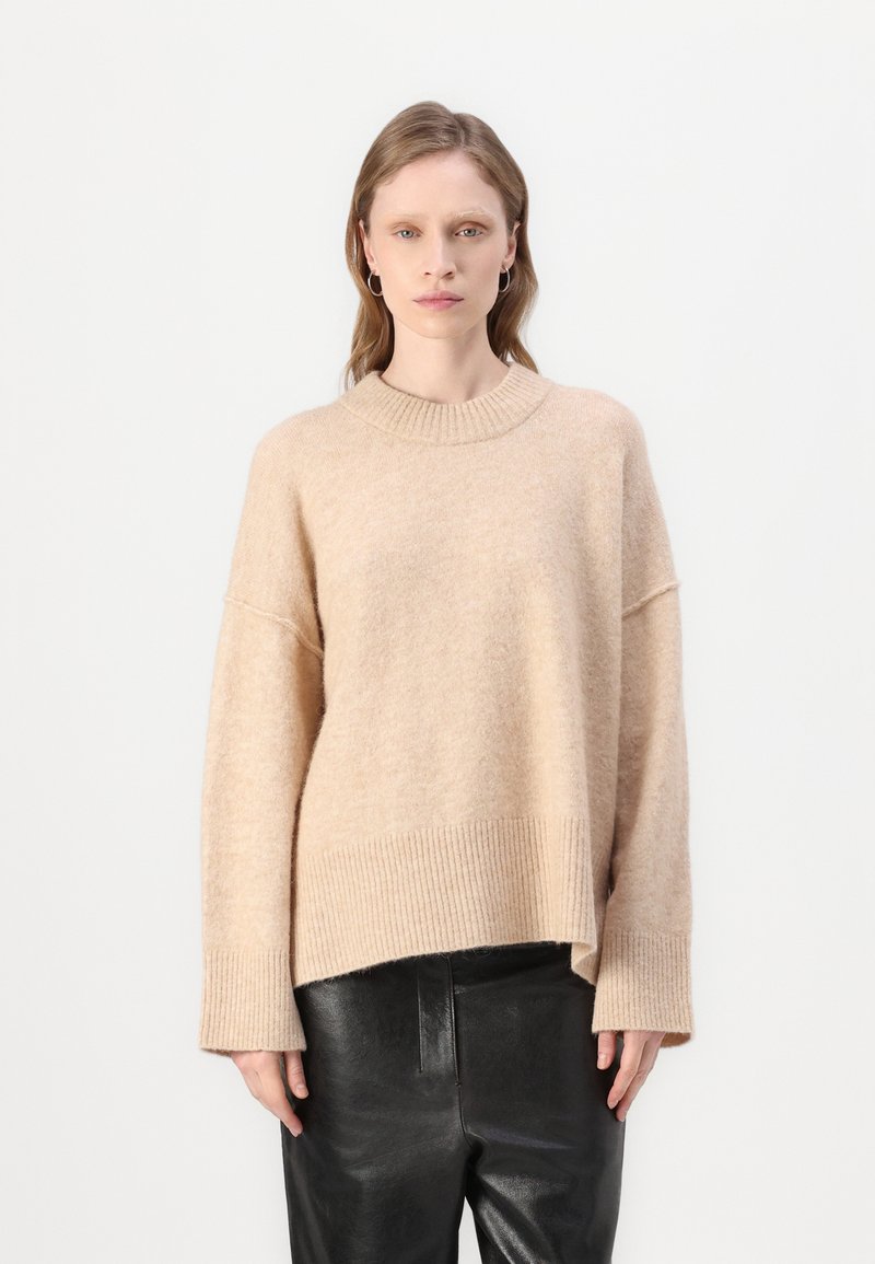 Beige oversized genser laget av myk, teksturert stoff. Har en ribbestrikket hals og mansjetter, og en avslappet passform som faller til hoften.