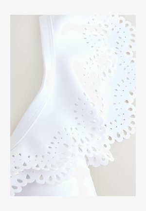 Fehér ruha bonyolult kivágott részletekkel a széleken, sima textúrával és strukturált dizájnnal a testhez álló megjelenésért.