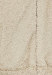 Tissu doux en fausse fourrure beige avec une couture verticale visible et une texture moelleuse, suggérant chaleur et confort.
