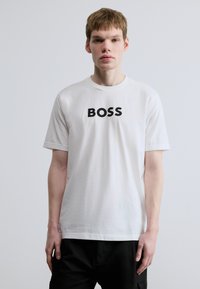 Valge puuvillane t-särk, mille esiküljel on julge must "BOSS" graafika. Lühikesed varrukad, ümarservane kaelus ja sirge alumine serv.