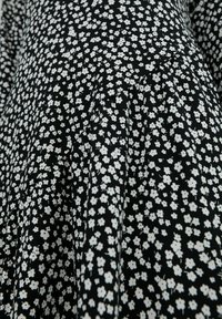 Svart tyg med ett litet vitt blommönster. Har en plisserad design med en mjuk textur och en enhetlig fördelning av blommor.