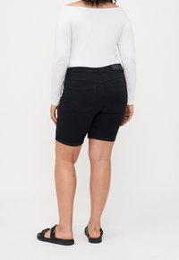 Mustat denimmitrikoiset bermudahousut, joissa on käännetyt lahkeet, istuva vyötärö ja takataskut. Yhdistetty valkoiseen pitkähihaiseen paita ja mustiin sandaaleihin.