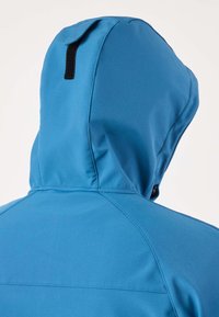 Vista posteriore di una persona che indossa una giacca con cappuccio blu in tessuto impermeabile e un anello nero sul cappuccio, su sfondo chiaro.