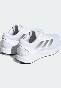 Baskets de course blanches avec une tige en mesh, un support de talon en plastique, des accents réfléchissants et une semelle rembourrée. Elles présentent trois bandes sur les côtés.