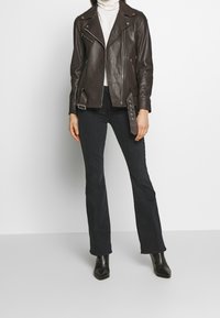 Brun lädermotorcykeljacka med notch-krage, dragkedjestängning och silverfärgade detaljer, tillsammans med mörka utsvängda jeans och svarta ankelstövlar.