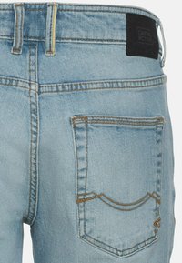 Light blue denim jeans with a classic five-pocket design, visible stitching, and a black brand label on the waistband.