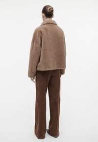 Bruine nepbontjas met een brede kraag, een relaxte pasvorm en lange mouwen, gecombineerd met bijpassende bruine tapered broeken.