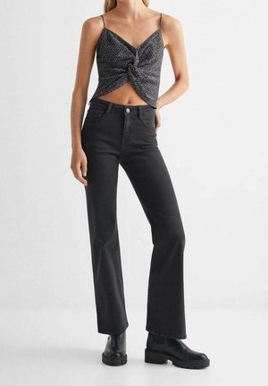 Jean noir à coupe évasée associé à un haut ajusté noué en tissu texturé. La tenue est complétée par des bottines noires épaisses.