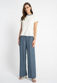 Biała, prążkowana bluzka z krótkim rękawem zestawiona z niebieskimi, wysokogatunkowymi spodniami dżinsowymi o szerokich nogawkach. Całość dopełniają błyszczące, srebrne sandały na paski.