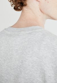Sweatshirt gris avec un tissu texturé, doté d'un col rond et de coutures visibles. L'accent est mis sur l'arrière du col et de l'encolure.