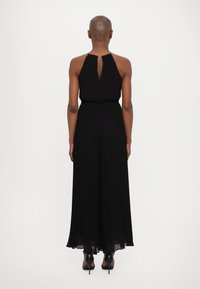 Musta plegeeritud jumpsuit kõrge kaelusega ja võtmeaugu selja detailiga, millel on sobiv talje ja laiad lõikejooned. Elegantne kangatekstuur.