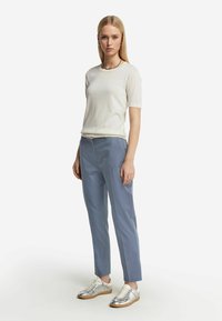 Ljust beige kortärmad topp i kombination med blå skräddarsydda byxor och silverfärgade sneakers. Outfiten har en minimalistisk design med subtil textur.