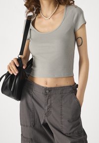 Šedý žebrovaný crop top s kulatým výstřihem, doplněný tmavě šedými volnými nákladními kalhotami s velkými kapsami, držený s černou kabelkou.