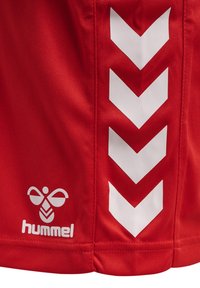 Rode sportshorts met witte chevronpatronen aan de zijkant en een wit "hummel" logo in de linksonderhoek. Glad materiaal.