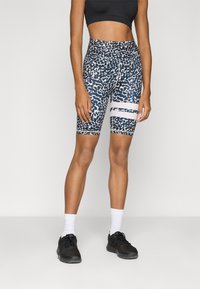 High-waisted bike shorts in navy with a white abstract pattern. Features white horizontal stripes and a fitted design. Paired with black athletic shoes.