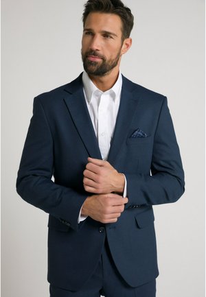 Marineblaues Sakko mit strukturiertem Finish, kombiniert mit einem frischen weißen Hemd. Das Einstecktuch weist ein dezentes Muster auf. Enganliegendes Design.