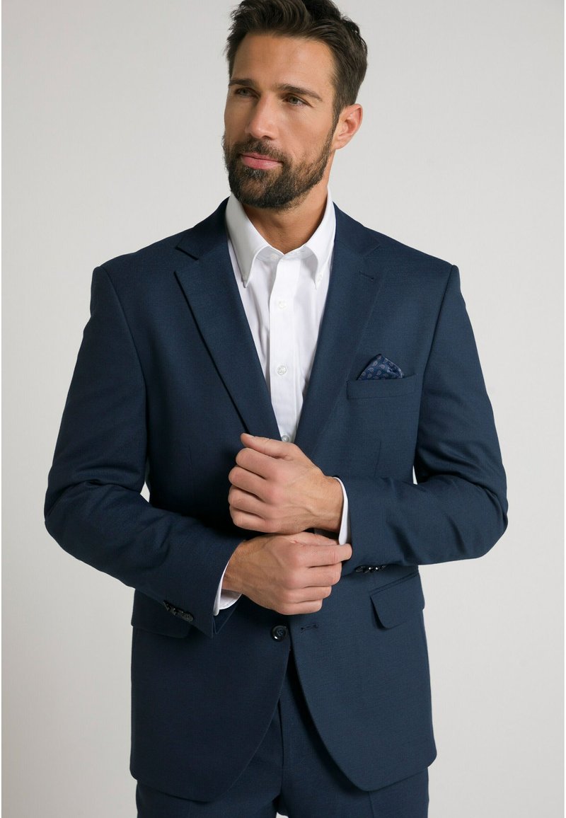 Giacca blu navy con una finitura testurizzata, abbinata a una camicia bianca brillante. Il fazzoletto da taschino presenta un motivo sottile. Design aderente.