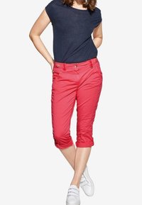 Red cropped pants with a smooth texture, rolled cuffs, and front pockets, paired with a navy short-sleeve top and white sneakers.