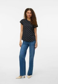 Zwarte t-shirt met polka dots en korte mouwen, gecombineerd met lichtblauwe rechttoe rechtaan spijkerbroek en beige pumps met spitse neus. Soepele stoftextuur.