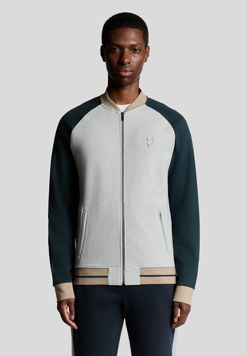 Graue zip-up Jacke mit dunkelgrünen Raglanärmeln und einem beigen Kragen. Verfügt über Seitentaschen und gestreifte Akzente am unteren Saum.