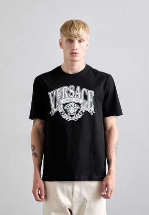 Black cotton T-shirt featuring a white graphic logo with a lion, "VERSACE" text, and floral accents. Short sleeves, relaxed fit.