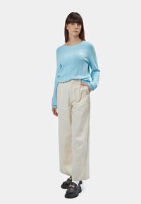 Maglione azzurro chiaro a maglia rasata abbinato a pantaloni crema a vita alta, completato da mocassini neri con catena dorata.