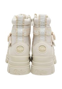 Beige high-top sneakers with glossy accents, textured fabric, padded collar, and distinct logo on the heel and straps.