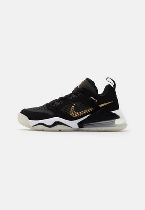 Sneakers basses noires et dorées avec panneau latéral en mesh, semelle blanche épaisse avec coussin d’air, lacets noirs et languette au talon.