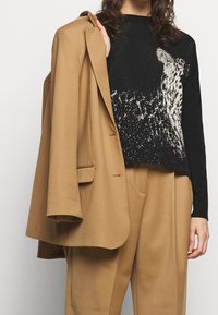 Czarny sweter w panterkę, noszony pod beżu marynarkę. Marynarka ma usztywnioną konstrukcję i luźny krój, który uzupełnia strój.