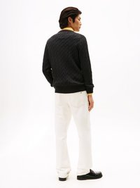 Μαύρο πλεκτό πουλόβερ με σχέδιο καλωδίωσης, λεπτομέρεια κίτρινου γιακά, συνδυασμένο με λευκά τζιν και μαύρα παπούτσια, απεικονίζεται από πίσω.