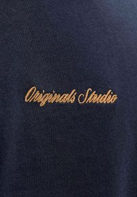 Tume siniste puuvillane T-särk peene tekstuuriga, millel on kuldne brodering, millel on stiliseeritud kiri "Originals Studio".