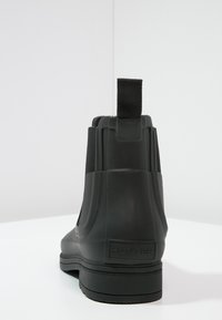 Bottines noires en caoutchouc avec panneaux élastiques sur les côtés, un talon texturé et une languette à l'arrière. Fini lisse avec logo de la marque.