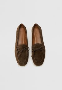 Mocassini in suede marrone con punta arrotondata, dettaglio con fiocco e frange sottili. Interno in pelle liscia con cuciture a contrasto. Suola piatta.