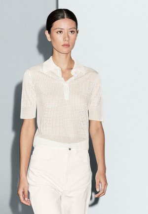 Lightweight, open-knit white polo shirt with short sleeves and a collar, paired with white pants. Textured pattern visible throughout.